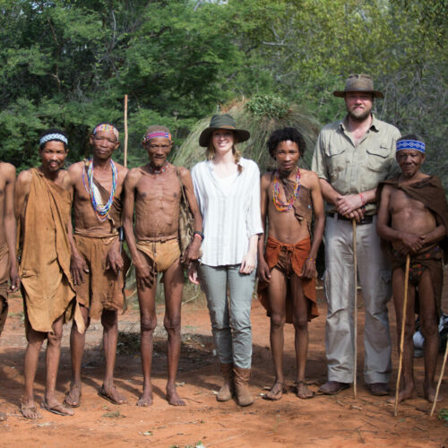 Two tourists from Golden Africa Safaris, standing with a group of Xaixai Khoi San in the bush