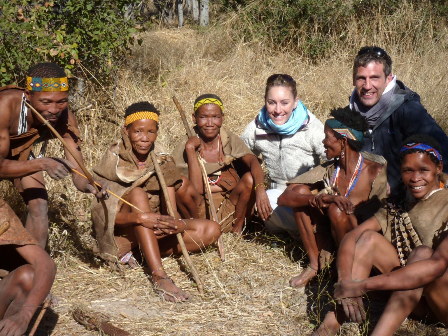 Two tourists from Golden Africa Safaris, seated with a group of Xaixai Khoi San in the bush